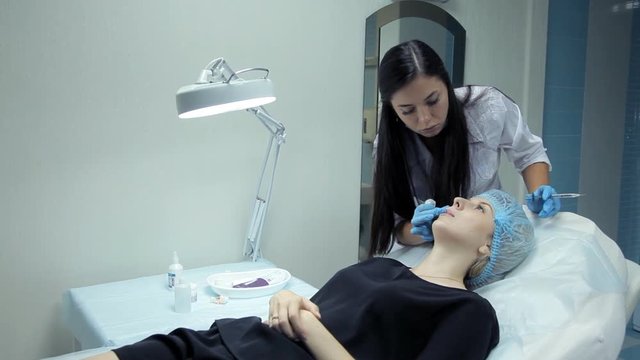 In the clinic, a medical cosmetologist injects Botox with a girl to increase her lips