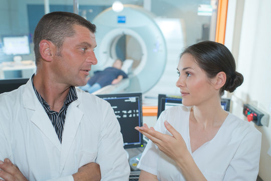 2 doctors talking with patient undergoing mri in the background
