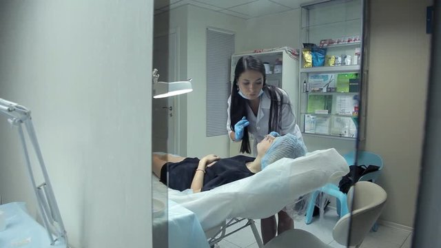 In the clinic, a medical cosmetologist injects Botox with a girl to increase her lips