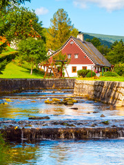 Small rustic mountain cottage and garden playground at small stream. Rural landscape on sunny day.