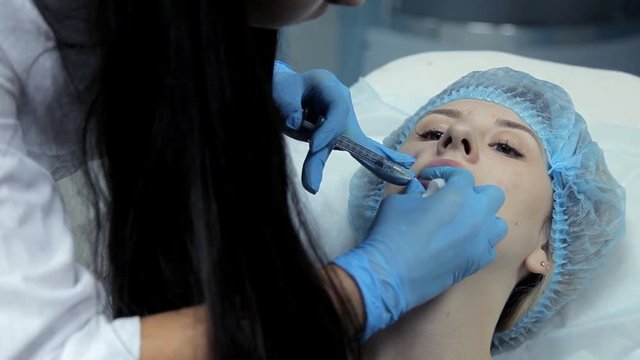 The doctor-cosmetologist makes the young girl lip enlargement procedures. Botox injection in the clinic.