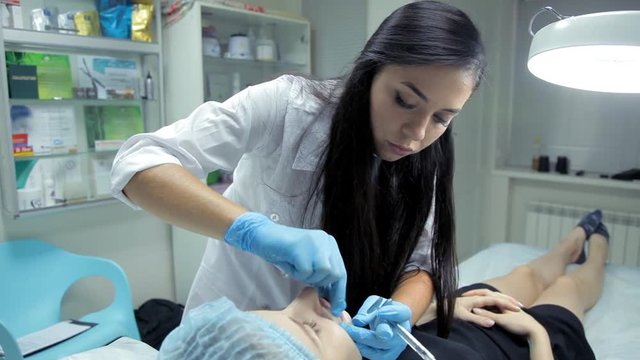 The beautician smoothes botox in the lips of a young girl after the injection. Lip augmentation procedure.