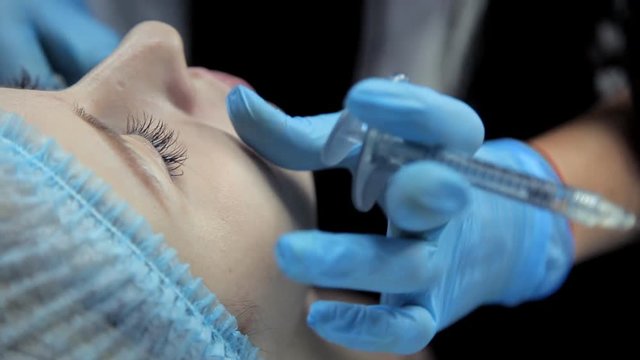 The beautician smoothes botox in the lips of a young girl after the injection. Lip augmentation procedure.