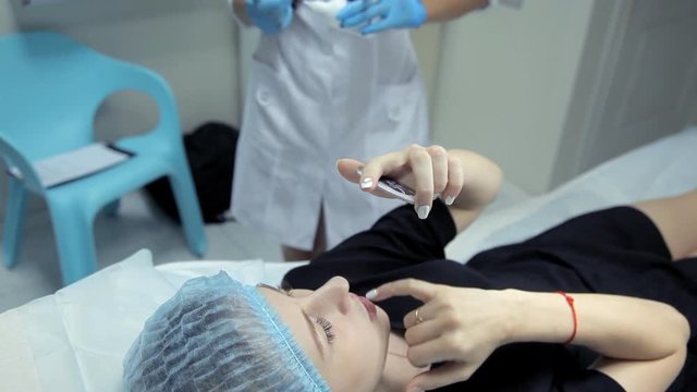 Young girl looks in the mirror after a lip augmentation procedure. Botox injection.