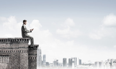 Man on roof edge send message with smartphone and cityscape at b