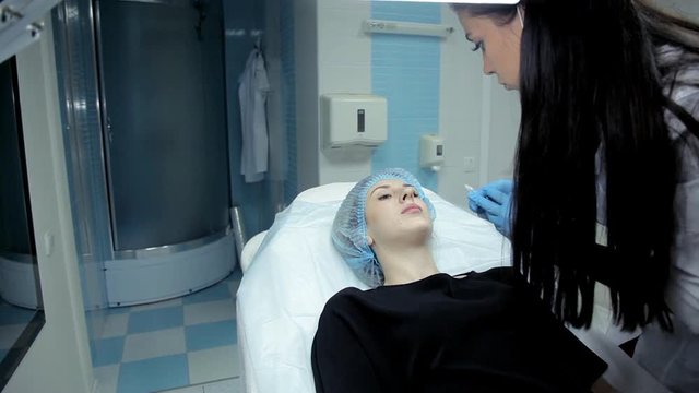 The doctor-cosmetologist makes the young girl lip enlargement procedures. Botox injection in the clinic.