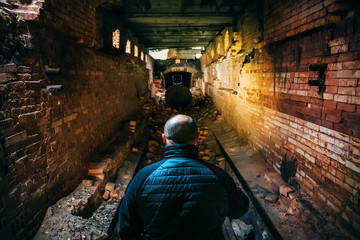 Man with flashlight in dark underground brick tunnel or corridor of abandoned brick factory, view from back, perspective