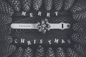 Rustic wooden background with pine cones. Merry Christmas. A smart watch as a gift with a bow. Black and white toning