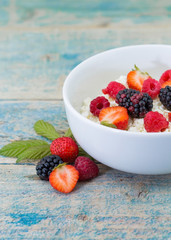 Organic cottage cheese with blackberry, strawberry and raspberry in a white ceramic bowl on the kitchen table. Dairy products for the breakfast. Healthy food concept.