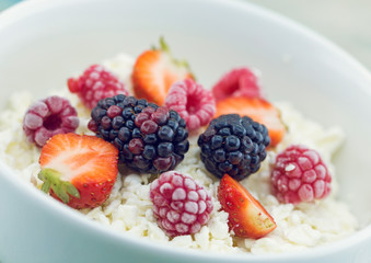 Organic cottage cheese with blackberry, strawberry and raspberry in a white ceramic bowl on the kitchen table. Dairy products for the breakfast. Healthy food concept.