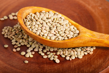 Pile of green lentils in a wooden spoon  on brown background.