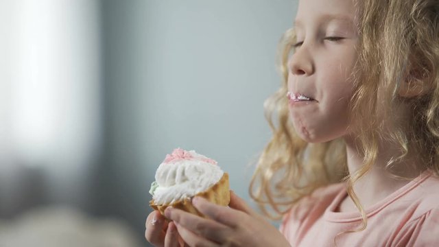 Close-up of pretty little girl biting cake and enjoying perfect taste of dessert