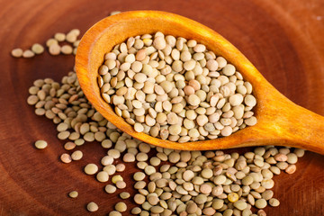 Pile of green lentils in a wooden spoon  on brown background.