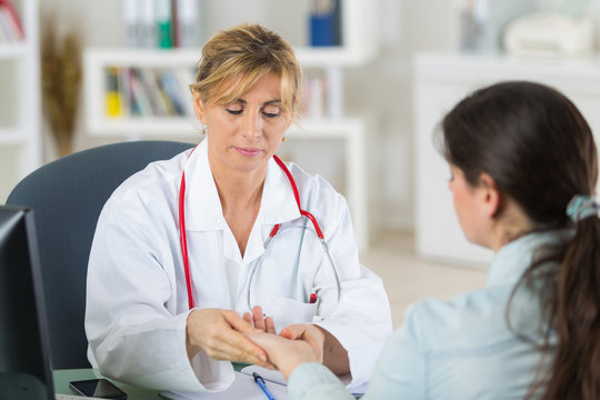 mature female doctor looking at her patients hands