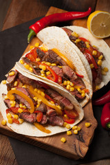 Three Mexican tacos with marbled beef, black Angus and vegetables on old rustic table. Mexican dish with sauces guacamole and salsa in bowls