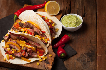 Three Mexican tacos with marbled beef, black Angus and vegetables on old rustic table. Mexican dish with sauces guacamole and salsa in bowls