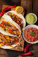 Three Mexican tacos with marbled beef, black Angus and vegetables on old rustic table. Mexican dish with sauces guacamole and salsa in bowls. top view