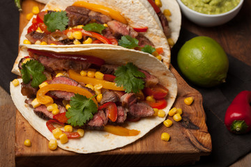 Three Mexican tacos with marbled beef, black Angus and vegetables on old rustic table. Mexican dish with sauces guacamole and salsa in bowls