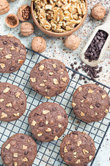 Homemade chocolate cookies with walnuts and chocolate chips on table and cooling rack, vertical, top view