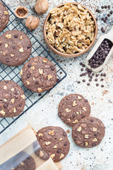 Homemade chocolate cookies with walnuts and chocolate chips on table and cooling rack, vertical, top view