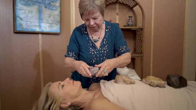 Energetic healer placing quarts and amethyst crystals on a mature woman&rsquo;s body for crystal dowsing therapy.