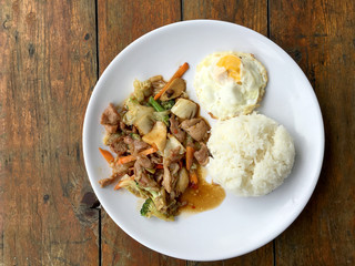 Thai spicy food : A plate of pork stir fry with vegetables and fried egg with rice in white dish on wooden table.  healthy dish.