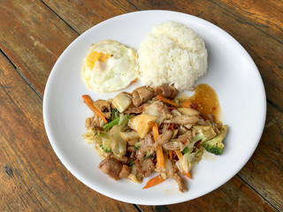 Thai spicy food : A plate of pork stir fry with vegetables and fried egg with rice in white dish on wooden table.  healthy dish.
