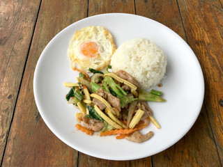 mixed vegetable stire-fried with meat and fried egg with rice in white dish on wooden background. Thai Food for health.