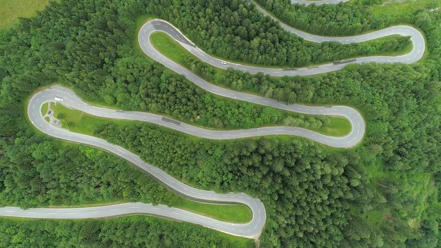 Aerial, top down cyclists and cars driving on scenic zig zag serpentine road through lush dense spruce forest on mountain slope