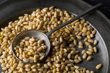 Heap of raw, uncooked pine nuts in metal spoon