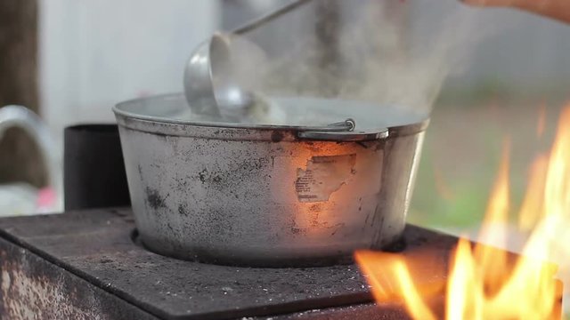 Cooking soup of fish in a metal pot on a wood-burning stove with an open fire