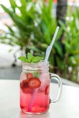 Refreshing iced strawberry lemonade in mason jar on a green nature background. Summer fresh concept.