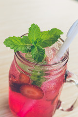 Refreshing iced strawberry lemonade in mason jar on a green nature background. Summer fresh concept.