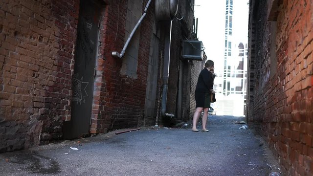 Nervous businesswoman walking down an alley making call to the police or husband