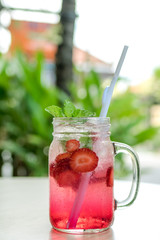 Refreshing iced strawberry lemonade in mason jar on a green nature background. Summer fresh concept.