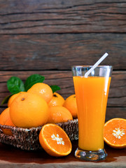 A glass of orange juice with a basket of oranges and the slices orange fruit with the wooden texture background.