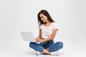 Photo of young smiling woman with long hair, holding and using laptop, while sitting with crossed legs
