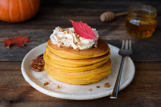 Pumpkin pancakes stack served with whipped cream, pecan nuts and cinnamon. Closeup view, horizontal, toned image
