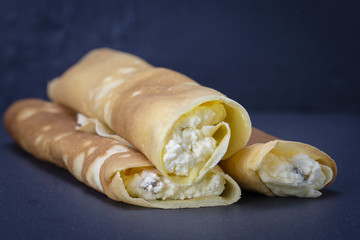 Homemade pancakes stuffed white cottage cheese with raisins on a black slate background, close up