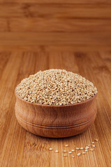 Quinoa in wooden bowl on brown bamboo board, close up. Healthy dietary groats  background.