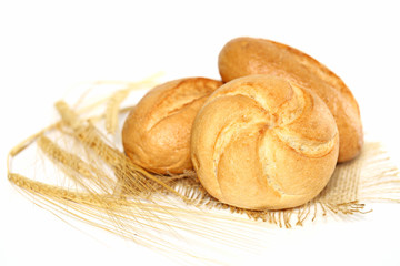 three fresh buns on sacking and wheat ear on white background