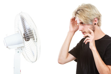 Young man fighting with wind from cooling fan