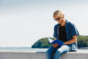 Sitting man reading book outside on sunny day