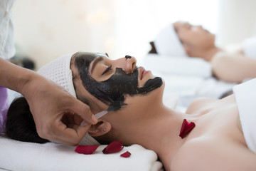 Beautiful woman getting facial black mud mask at beauty salon.