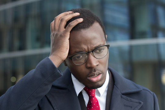 Horizontal headshot of young dark-skinned businessman standing outdoors with facepalm gesture, touching head with palm with puzzled and worried face expression