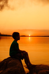 A little boy is sitting on the rocks. Beautiful summer sea sunset.
