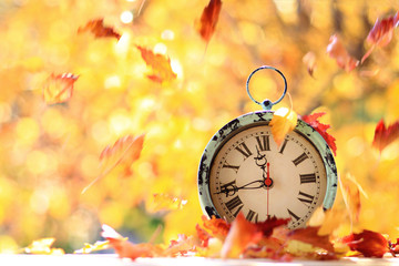 Autumn leaves blowing in the wind across an antique alarm clock