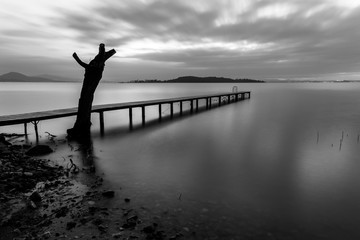 Fototapeta premium Long exposure view of a pier on a lake, with moving clouds and perfectly still water
