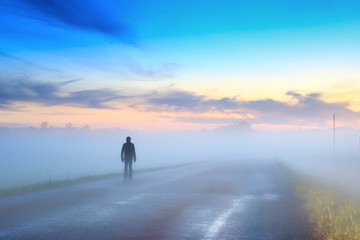Silhouette of a man walking on the road in the fog at sunset
