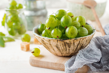 Fresh raw gooseberry berries in  white ceramic plate on light wooden background. Selective focus. Rustic style.